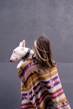 Rear view of woman in colorful poncho carrying bull terrier