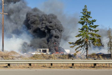 Billowing black smoke from burning tires at commercial site, caught in a brush fire.