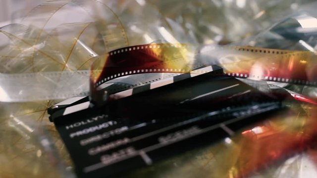 Concept of vintage movie, reel and clapper on unrolled transparent filmstrip right to left panning