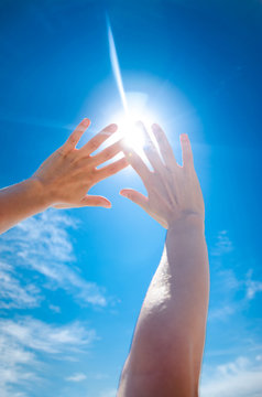 Two palms cover from the sun. First-person view of the sky. Sun is shining through fingers