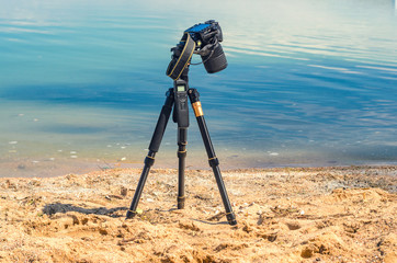 Camera on a tripod near the seaside removes of seashells on the sand. Photographic equipment in the...