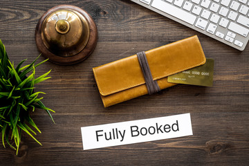 Book hotel online. Bank card and purse near service bell and keyboard on dark wooden table...