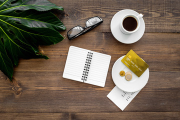 Pay restaurant bill. Bill, bank card, coins near cup of coffee on dark wooden table top view