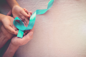 Adult and child hands holding Teal Ribbon, toning background, Ovarian Cancer, cervical Cancer,...
