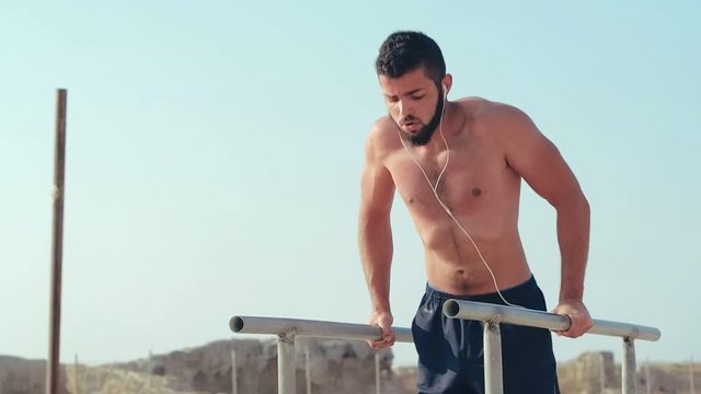 Bearded athlete in headphones pressing on parallel bars. Power training