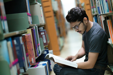Asian student in the library at bookshelf.She is reading