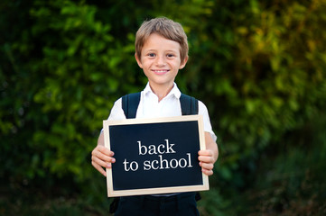 Back to school concept. Elementary school student boy holding blackboard background. Cute caucasian primary grade pupil in for first day in education semester