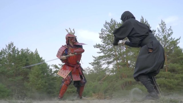 Ninja in a black kimono and a samurai in red armor are fighting on katanas in the forest, bit slow motion