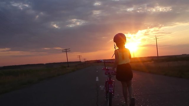 Little girl having fun riding bike at sunset, active family sport, active kids sport, Silhouette a kid at the sunset, Moments of family happiness. Orange-blue sky background.