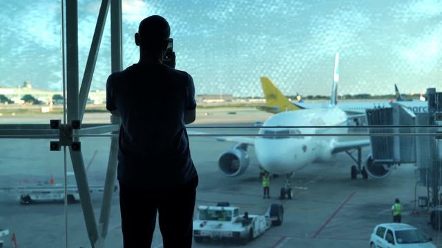 Silhouette of man taking photos with cellphone in lobby at airport 
