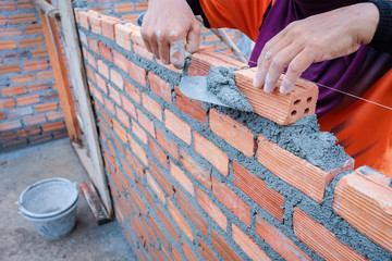 The hands of the construction workers are building a brick red brick wall