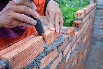 The hands of the construction workers are building a brick red brick wall