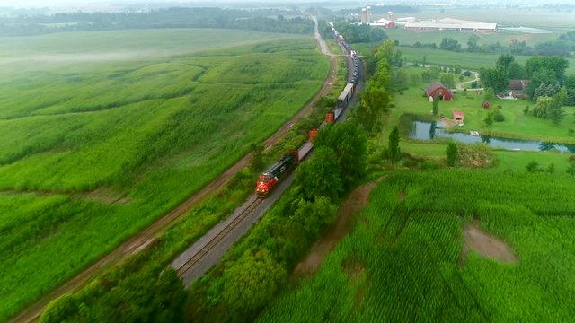 Train rolling through foggy rural countryside at dawn, aerial perspective.
