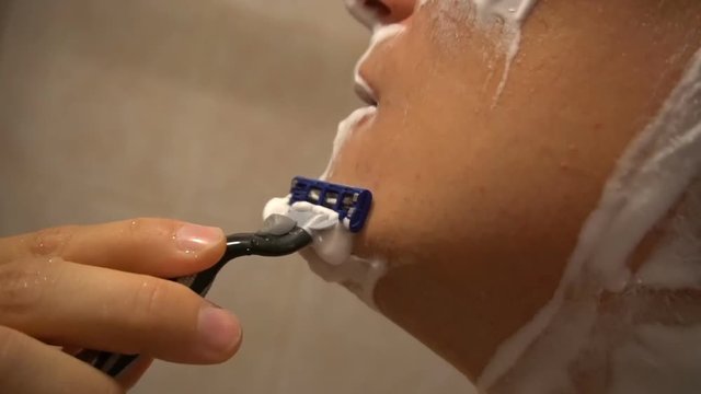 Adult man shaving with foam and manual razer.