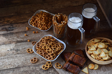 Football fan set with mugs of beer and salty snacks on wooden background. Crackers, pretzel, salted straws, nuts, dried fish. Junk food for beer or cola. Photographed with natural light.