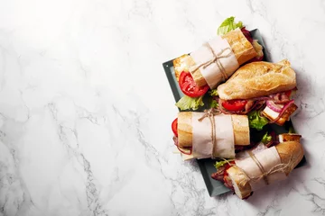Zelfklevend Fotobehang Fresh baguette sandwich bahn-mi styled. Bacon, roasted cheese, tomatoes and lettuce on metallic tray on white marble background. © Anastasiia Nurullina