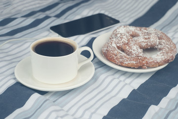 Cup of coffee with fresh bakery and a phone on bed background