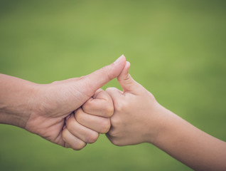 Closeup mother and son are hand thumb up in green background. People, charity and family concept.