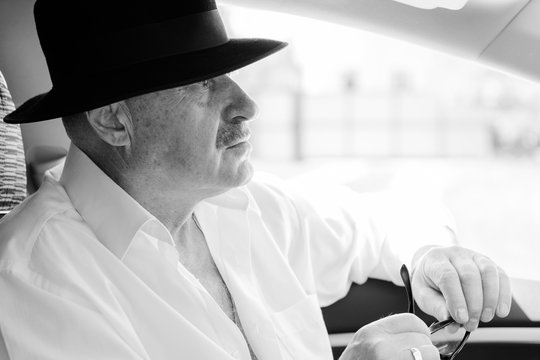 Mature Stylish European Or American Man Wear Black Hat, Glasses And White Shirt Driven Car, Modern And Hipster Style For Older People. Such A Good Mood At Pretty Day