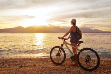Fototapeta na wymiar Traveler with bike enjoying the sunset on the background of the island