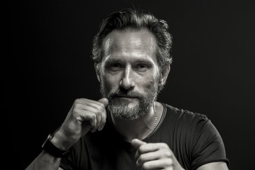 Black and white portrait of self confident brutal man. Mid aged male showing fists on black background.