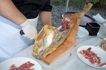 Professional cutter carving slices from a whole bone-in serrano ham