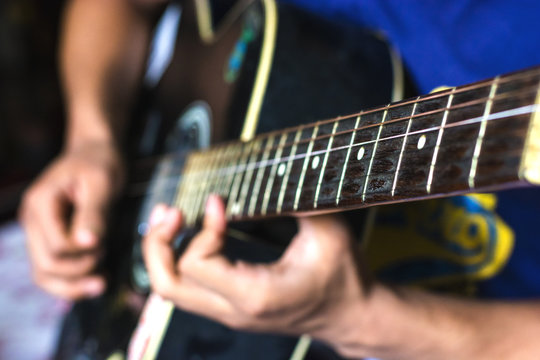blurred background of a guy wearing blue T-shirt playing his guitar
