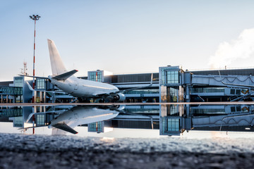 Fototapeta premium Passenger aircraft parked to a jetway with reflection in a puddle