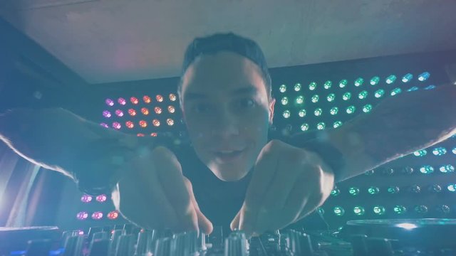 A DJ in close view turns knobs with both hands. 