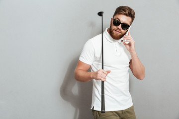 Calm golfer talking by the smartphone and holding club