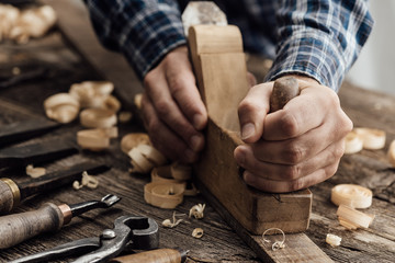 Carpenter working in his workshop, he is smoothing a wooden board using a planer, carpentry, carpentry, woodworking and craftsmanship concept