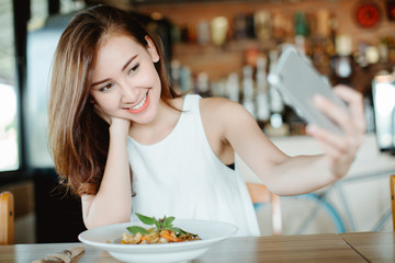 Young Asia woman eating spaghetti at restaurant and using smart phone for selfie