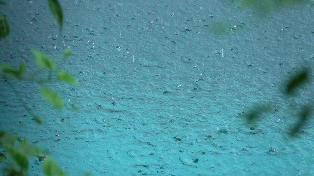 SLOW MOTION, CLOSE UP: Raindrops falling in ocean creating a pattern of circular waves on water surface. Summer monsoon during the rain season in tropics. Waterdrops splashing in circles in the pool