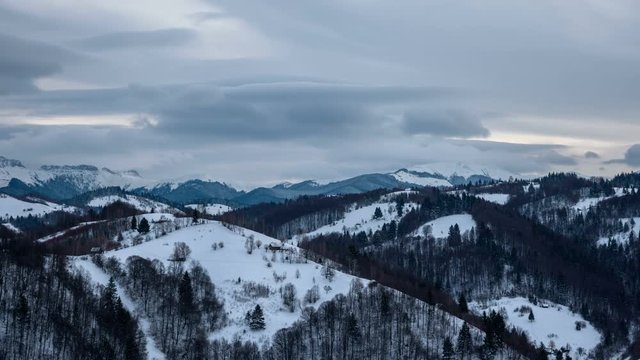 Winter Transylvanian landscape near Bran at sunset. Mountain countryscape during winter with grey clouds and isolated houses. 4k timelapse. 