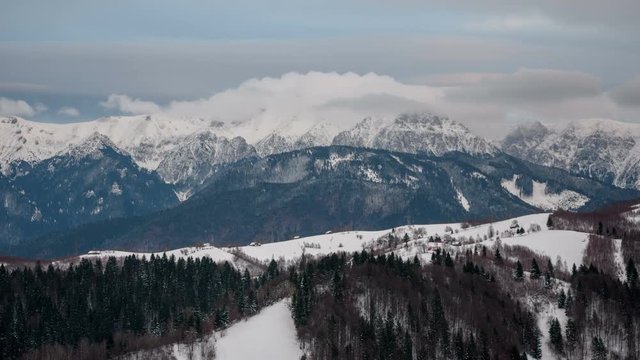 Dynamic white clouds over Bucegi Mountains in winter. 	Mountains view in background and isolated houses in foreground. 4k timelapse. 
