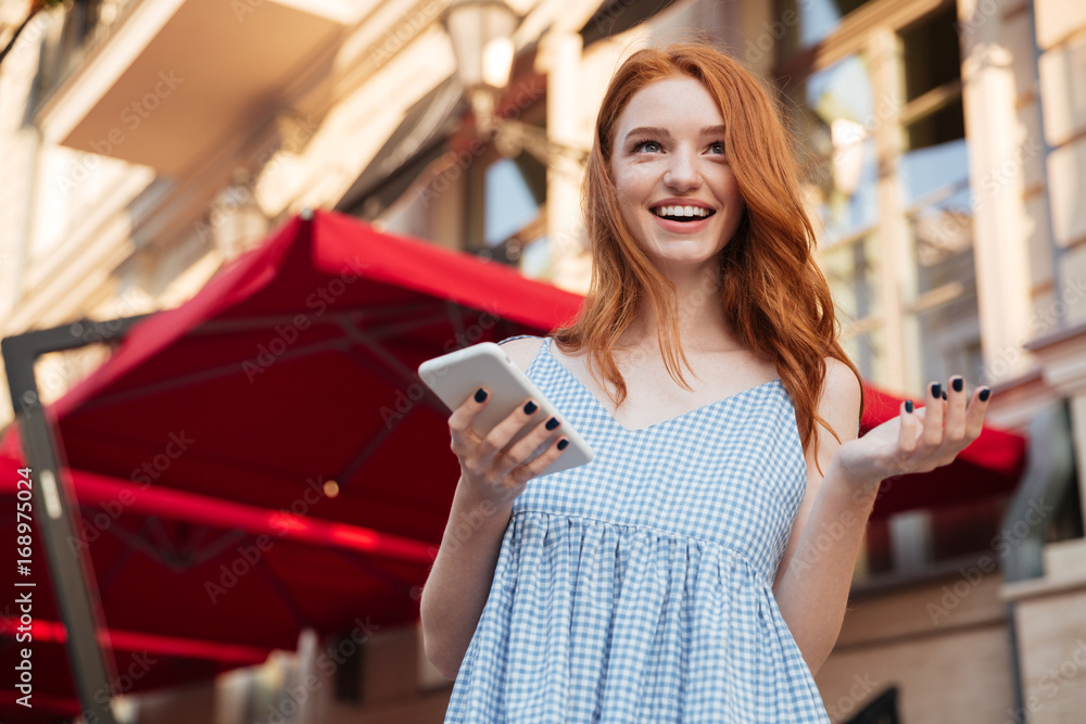 Poster excited young redhead girl holding mobile phone