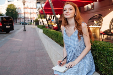 Smiling redhead girl holding notepad and a pen