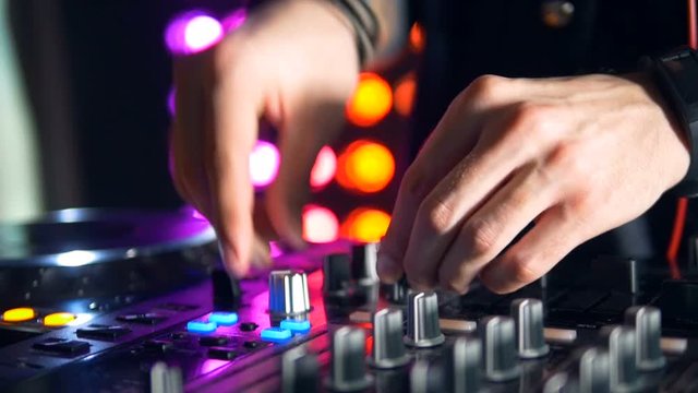 DJs hands twist a turntable and add volume. 