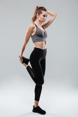 Fototapeta premium Portrait of a young fitness woman stretching leg while standing