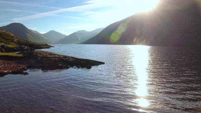 Wast water low tracking shot with sun glare and the mountains in the distance.