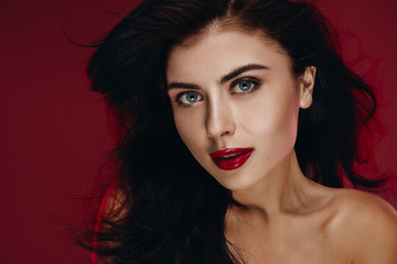 Fototapeta premium Beauty Brunette Woman with Perfect Makeup. Beautiful Professional Holiday Make up. Beauty Girl Face studio portrait isolated on red background