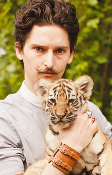 A man with a mustache looks into the face of a tiger cub