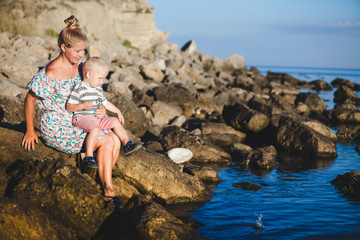 Mom and son are sitting on the stones on the beach and smiling