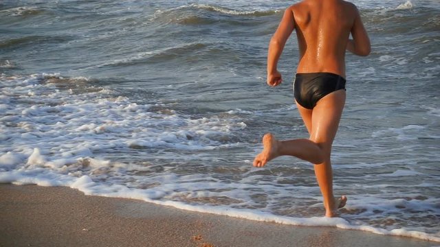 Teenage boy running to the sea from beach