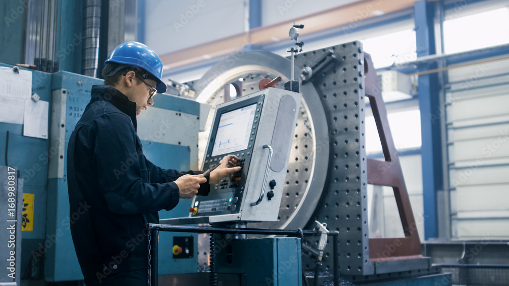 Fototapete Factory worker is programming a CNC milling machine with a tablet computer.
