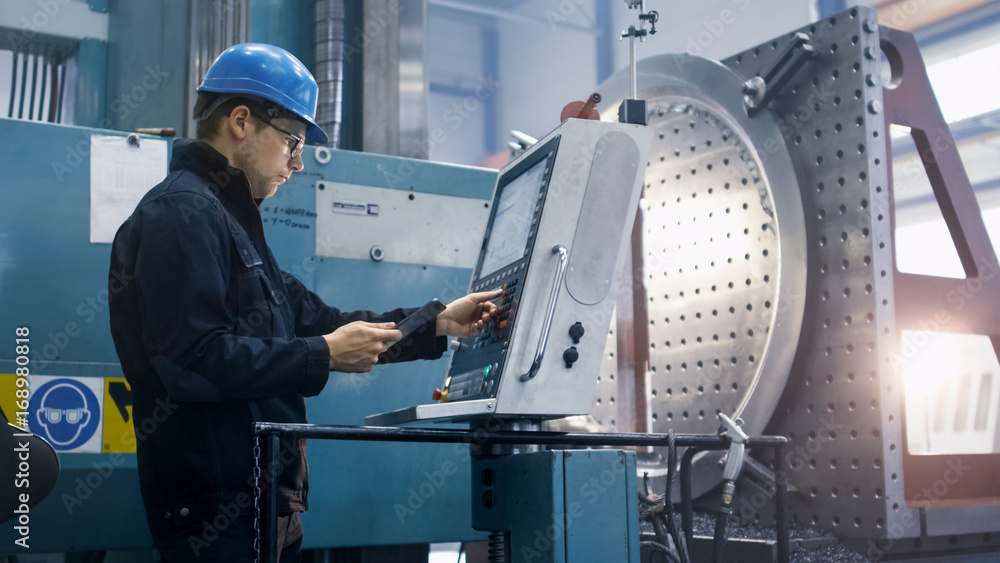 Fototapete Factory worker is programming a CNC milling machine with a tablet computer.
