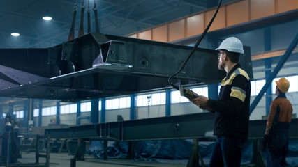 Heavy industry workers are moving a massive metal construction object in a factory.