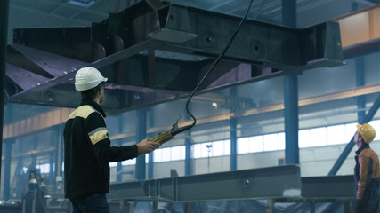Heavy industry workers are moving a massive metal construction detail in a factory.