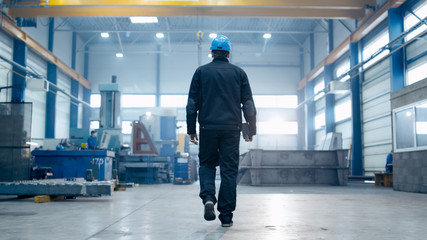 Factory worker in a hard hat is walking through industrial facilities.