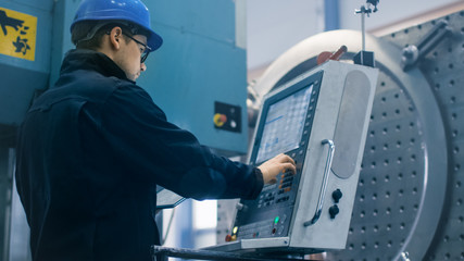Factory worker is programming a CNC milling machine with a tablet computer.